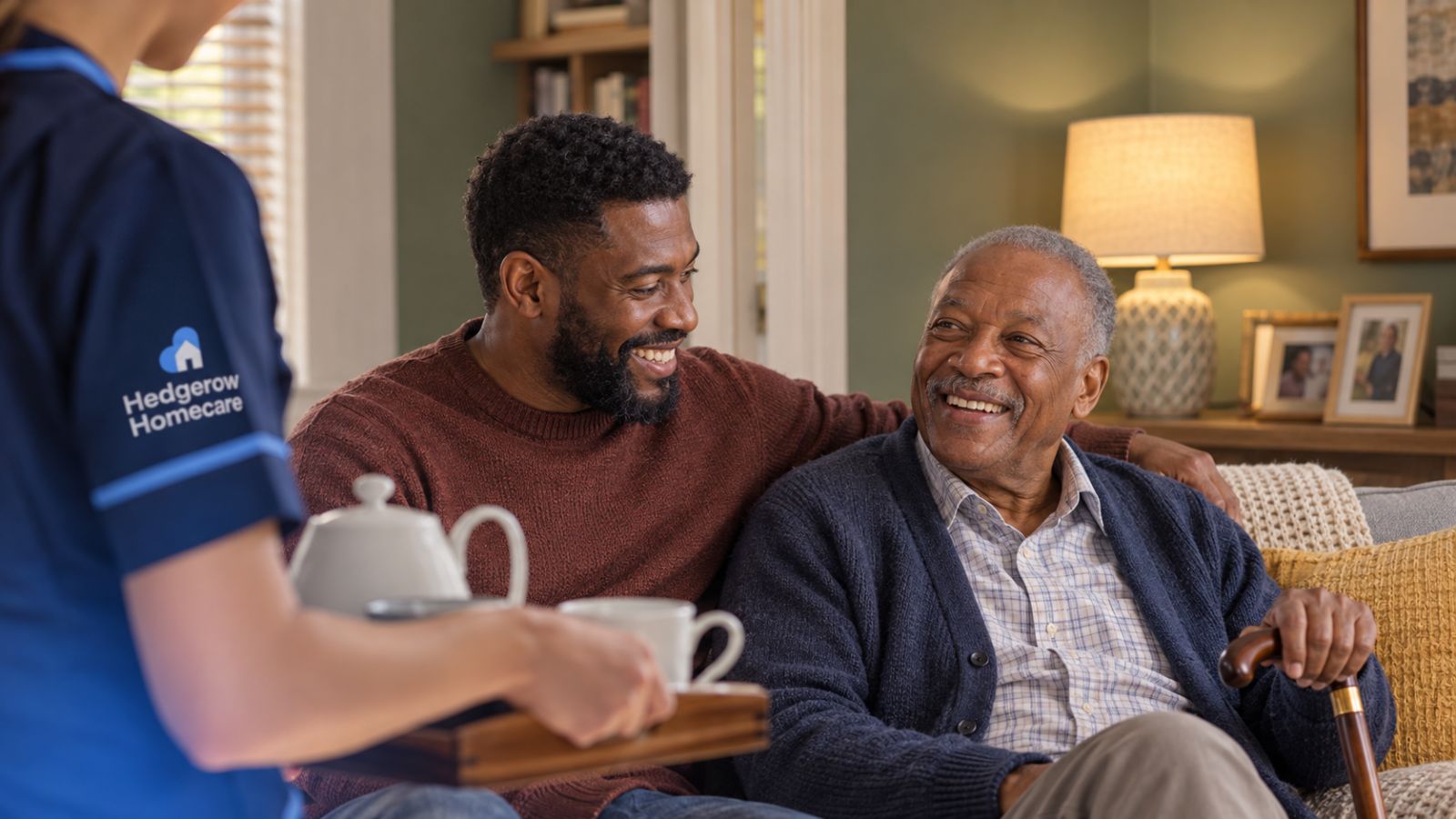 A carer bringing tea to an older man and his son at home